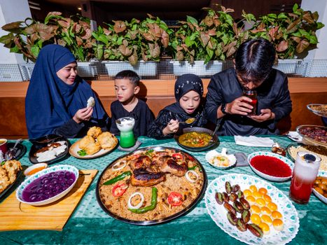A joyful family gathering around a table full of traditional iftar delicacies during Ramadan.