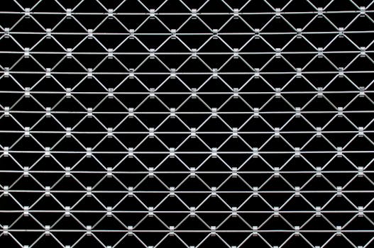 Close-up view of a symmetrical metal wire fence creating a geometric pattern against a dark background.