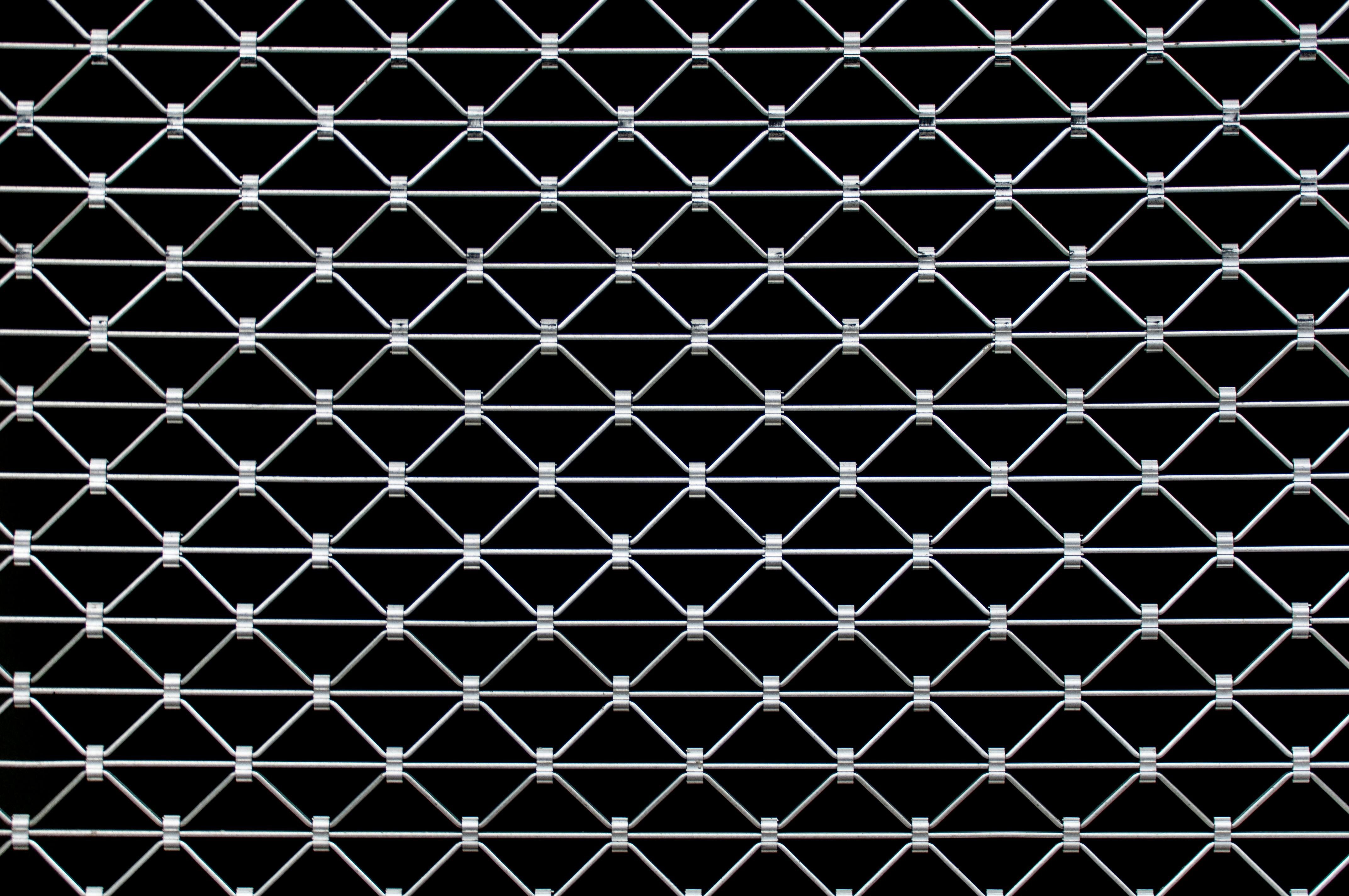 Free Close-up view of a symmetrical metal wire fence creating a geometric pattern against a dark background. Stock Photo