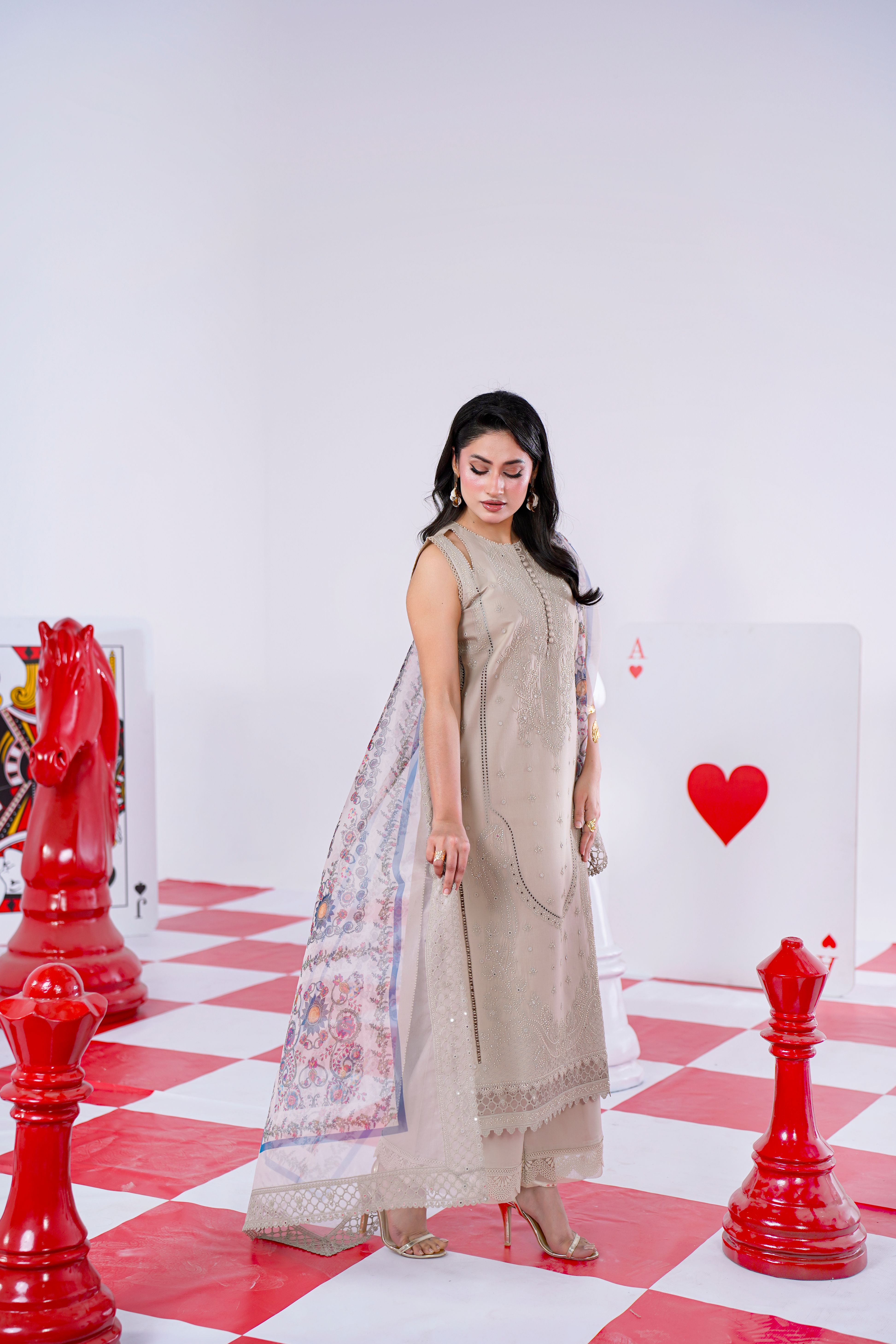 Model posing in embroidered Eastern dress on chess-themed set in Lahore studio.