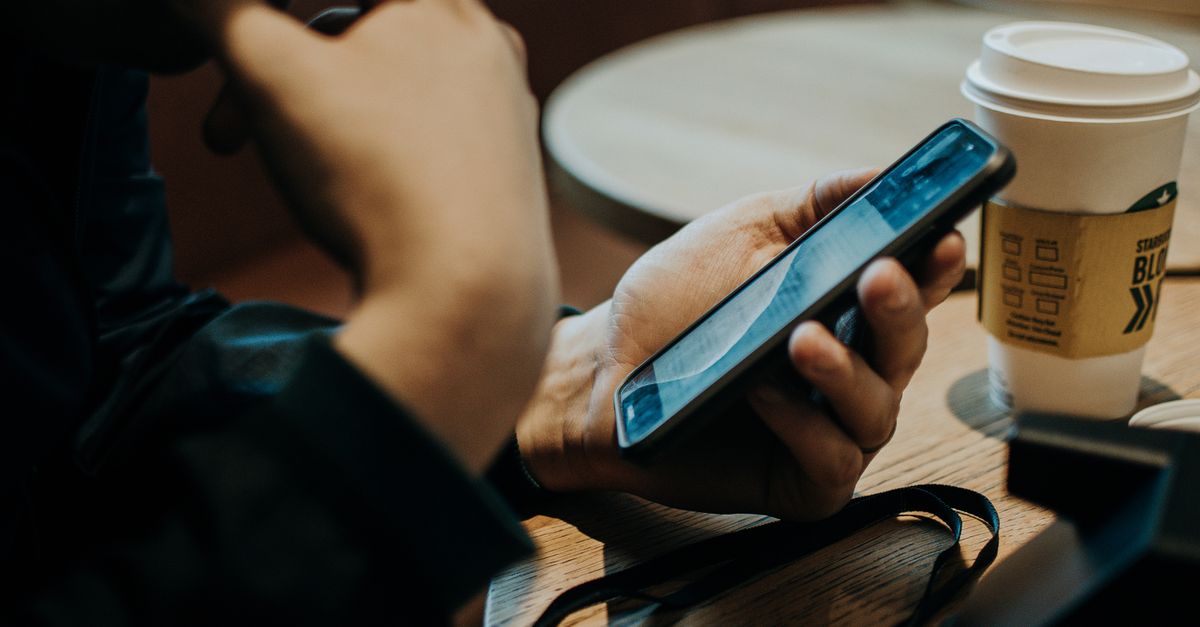 Mani che tengono uno smartphone accanto a una bevanda in un caffè.
