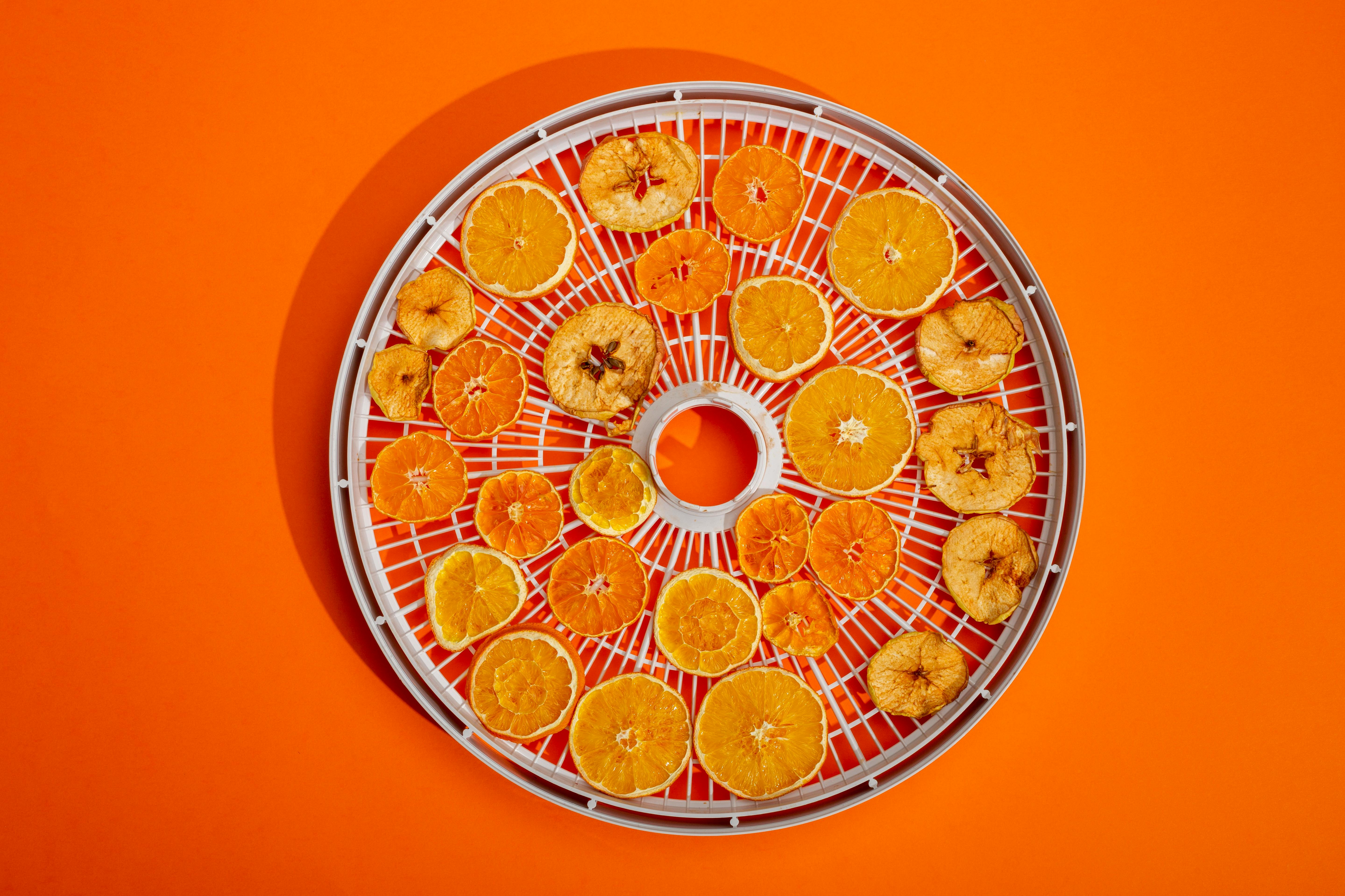 Gratis En samling tørrede citrusskiver på et rundt tørrestativ med en lys orange baggrund. Lagerfoto