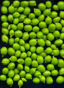 Close-up of vibrant green peas scattered on a dark surface, showcasing fresh produce in detail.