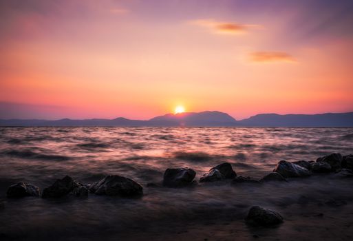 Dramatic sunset over a calm sea with rocky shoreline. Captivating colors and peaceful atmosphere.