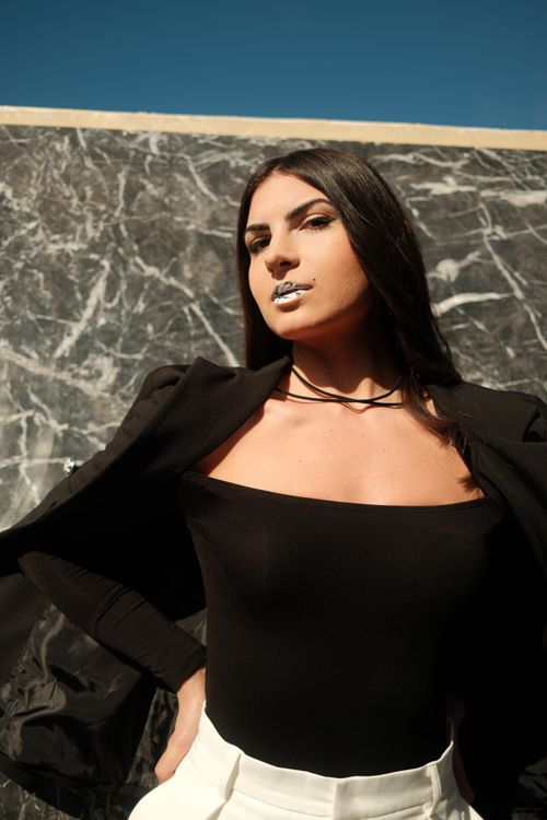 Free Portrait of a stylish woman in black attire posing confidently against a marble wall under bright daylight. Stock Photo
