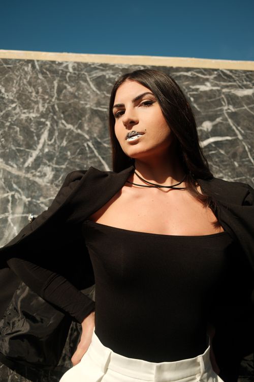 Free Portrait of a confident woman in a black outfit striking a pose against a marble wall. Stock Photo