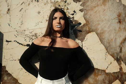 Striking fashion portrait of a woman with bold makeup, standing outdoors against a textured wall.