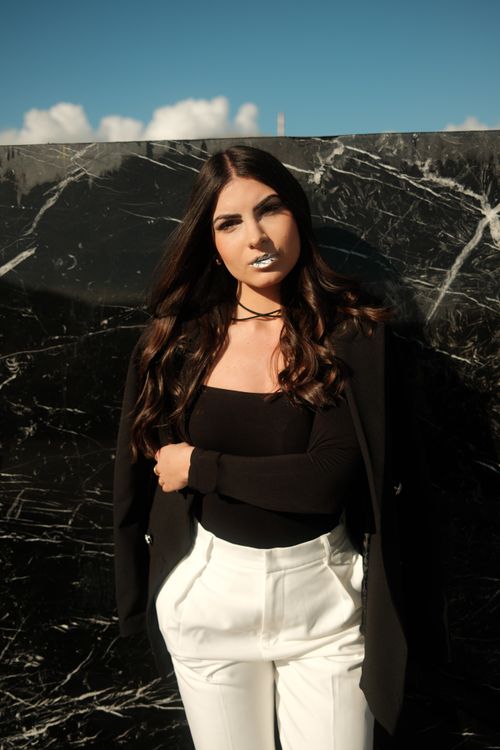 Free Confident woman posing in chic black and white outfit against a marble textured wall under clear sky. Stock Photo