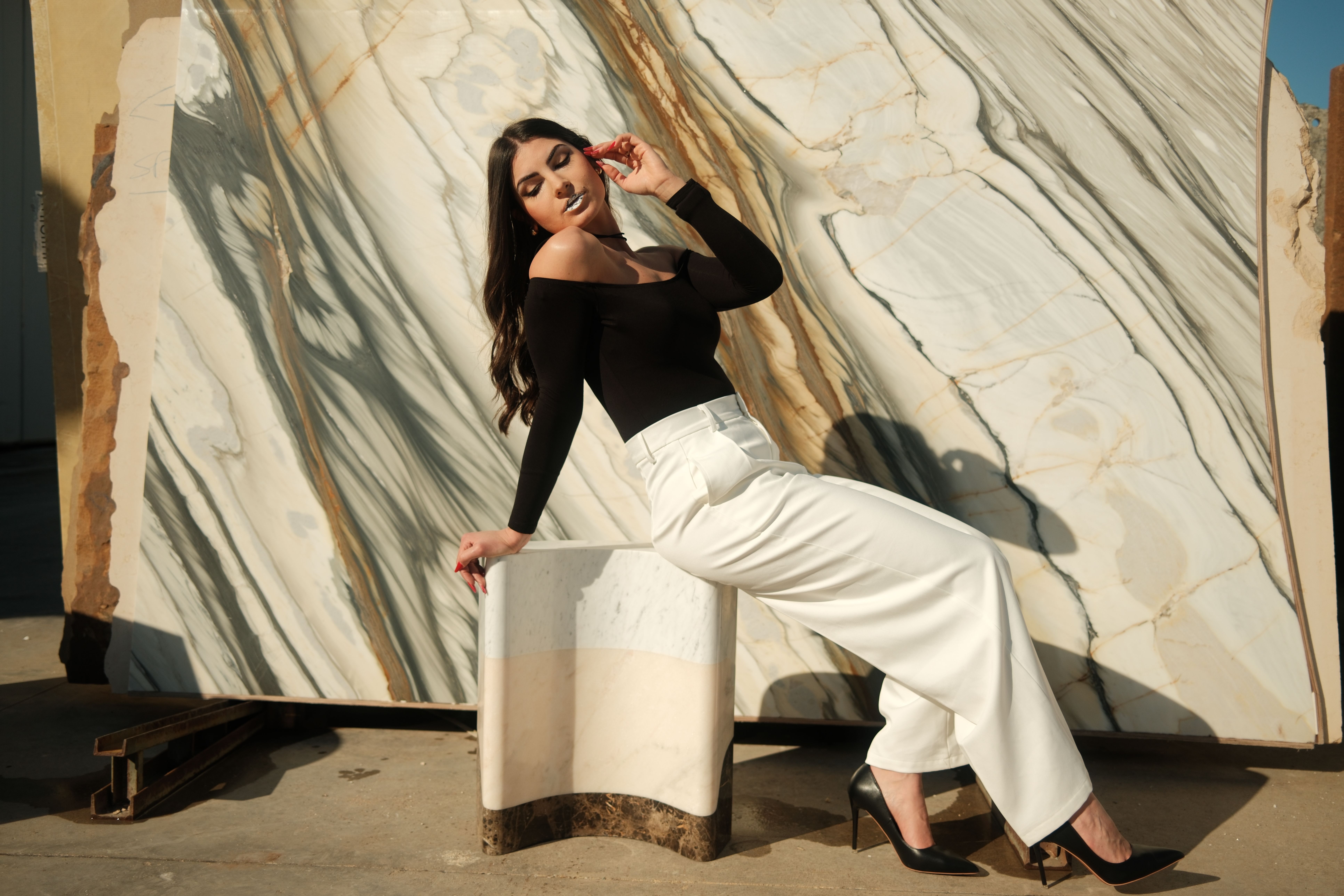 Stylish woman in chic outfit poses against marble backdrop in outdoor setting. Perfect for lifestyle and fashion themes.