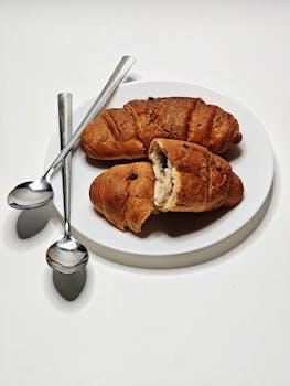 Delicious chocolate croissants served on a white plate with spoons, perfect for breakfast or a snack.