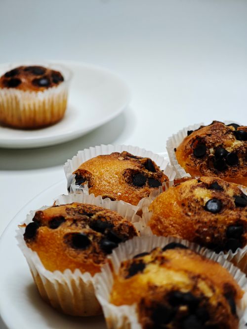 Free Close-up of freshly baked chocolate chip muffins in white paper liners on white plates. Stock Photo