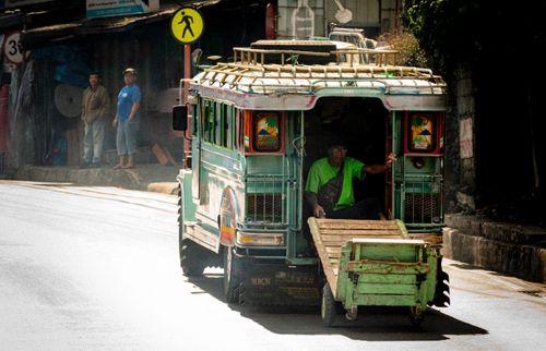Free A traditional Filipino jeepney traveling through a bustling urban street in Manila on a sunny day. Stock Photo