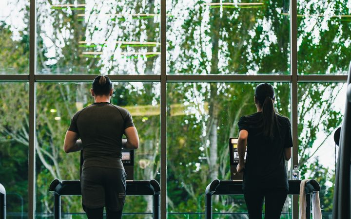 Two fitness enthusiasts running on treadmills in a gym with outdoor view.