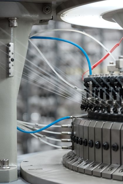 Máy dệt kim công nghiệp đang chạy, nhiều sợi trắng được dẫn vào cụm kim để tạo vòng sợi
