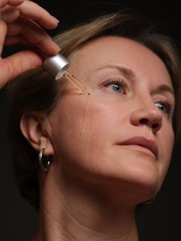 Close-up of woman applying facial serum with a dropper, focusing on skincare and beauty.