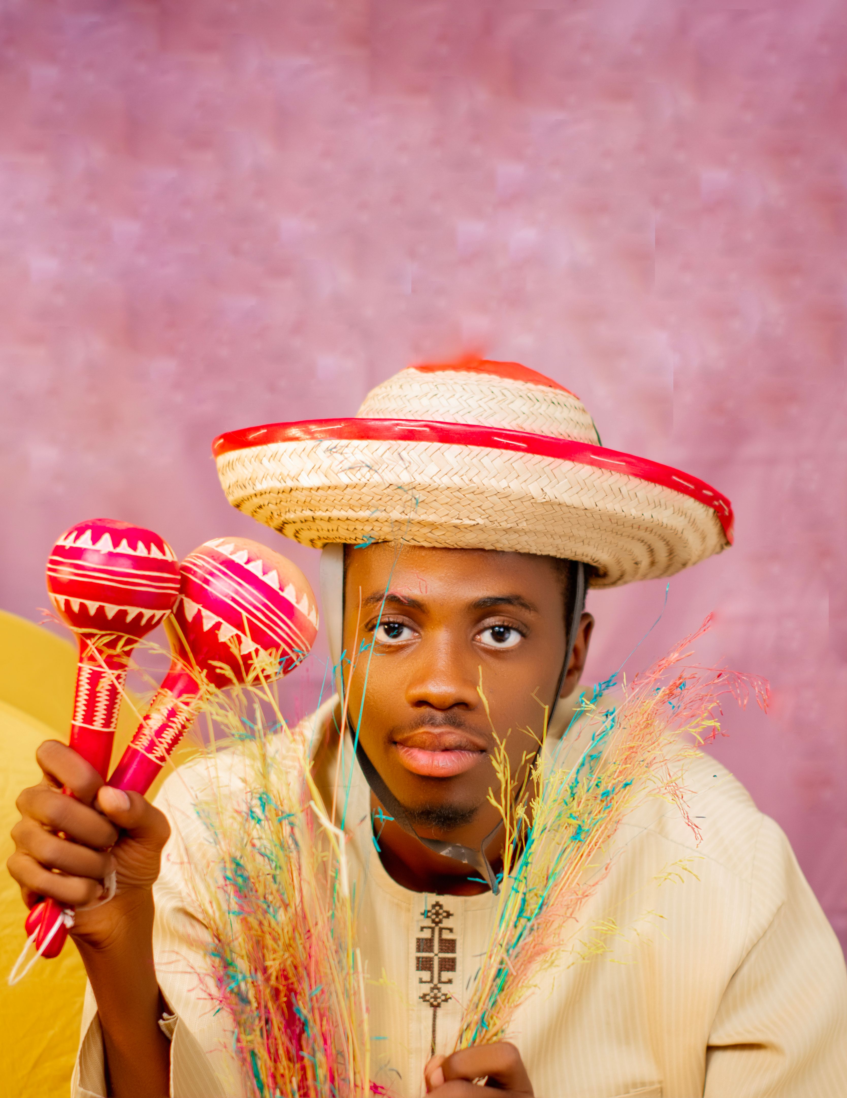 Portrait of a young man wearing a traditional hat, holding maracas and colorful decorative grass.