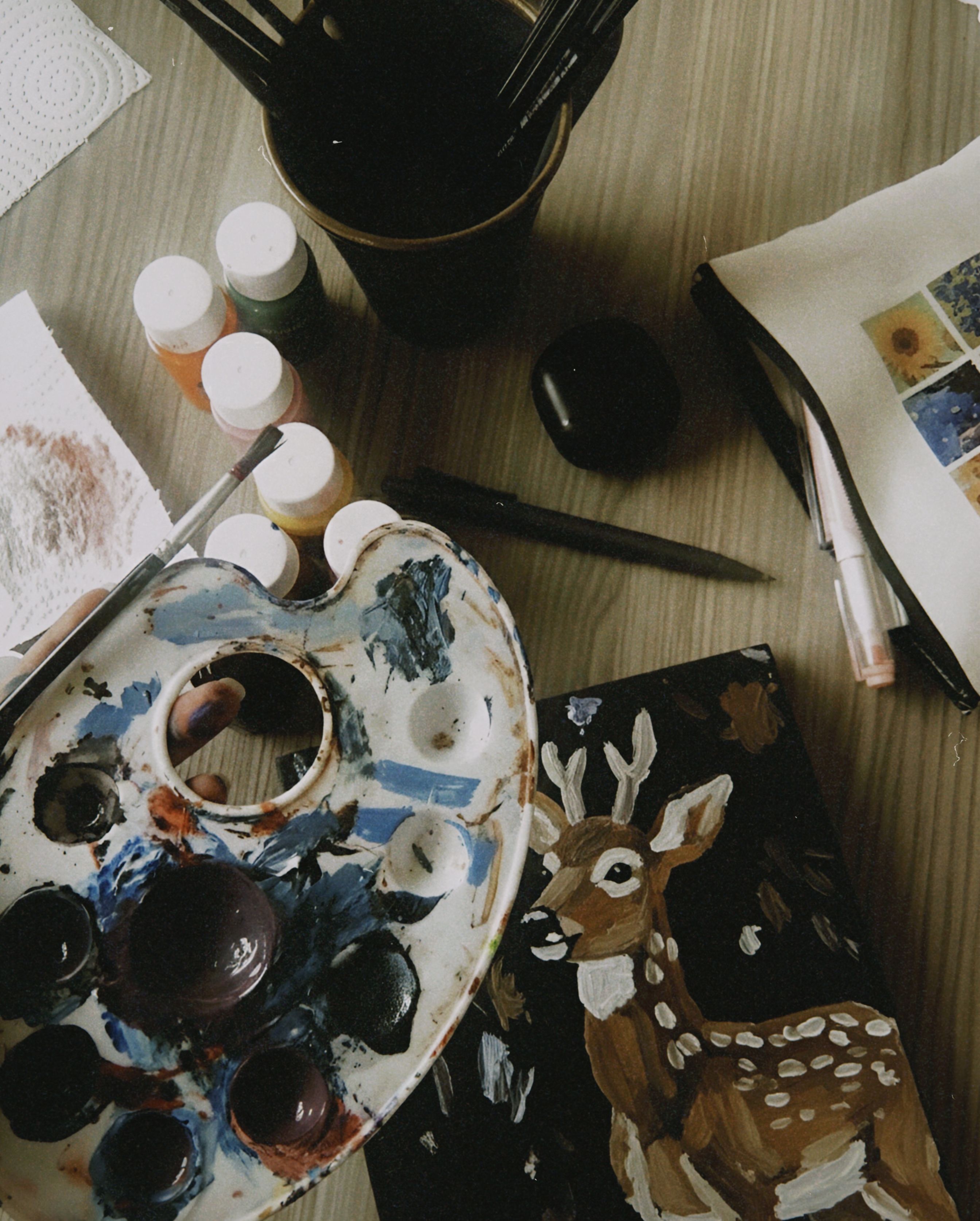 Artistic workspace featuring a deer painting, paint palette, and brushes for creativity.