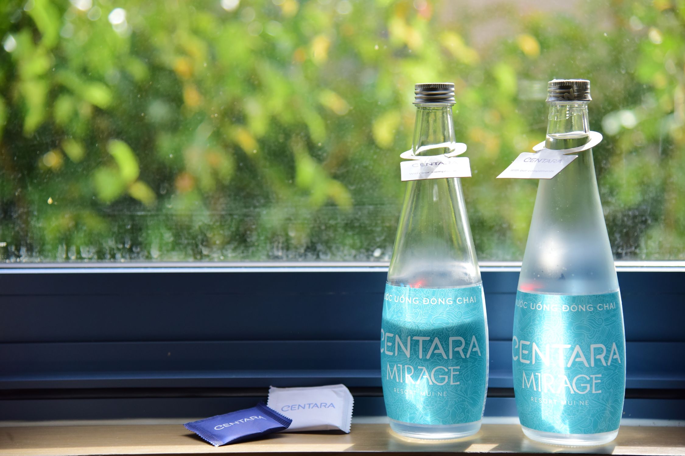 Two bottles of Centara Mirage water on a window sill with green foliage background.