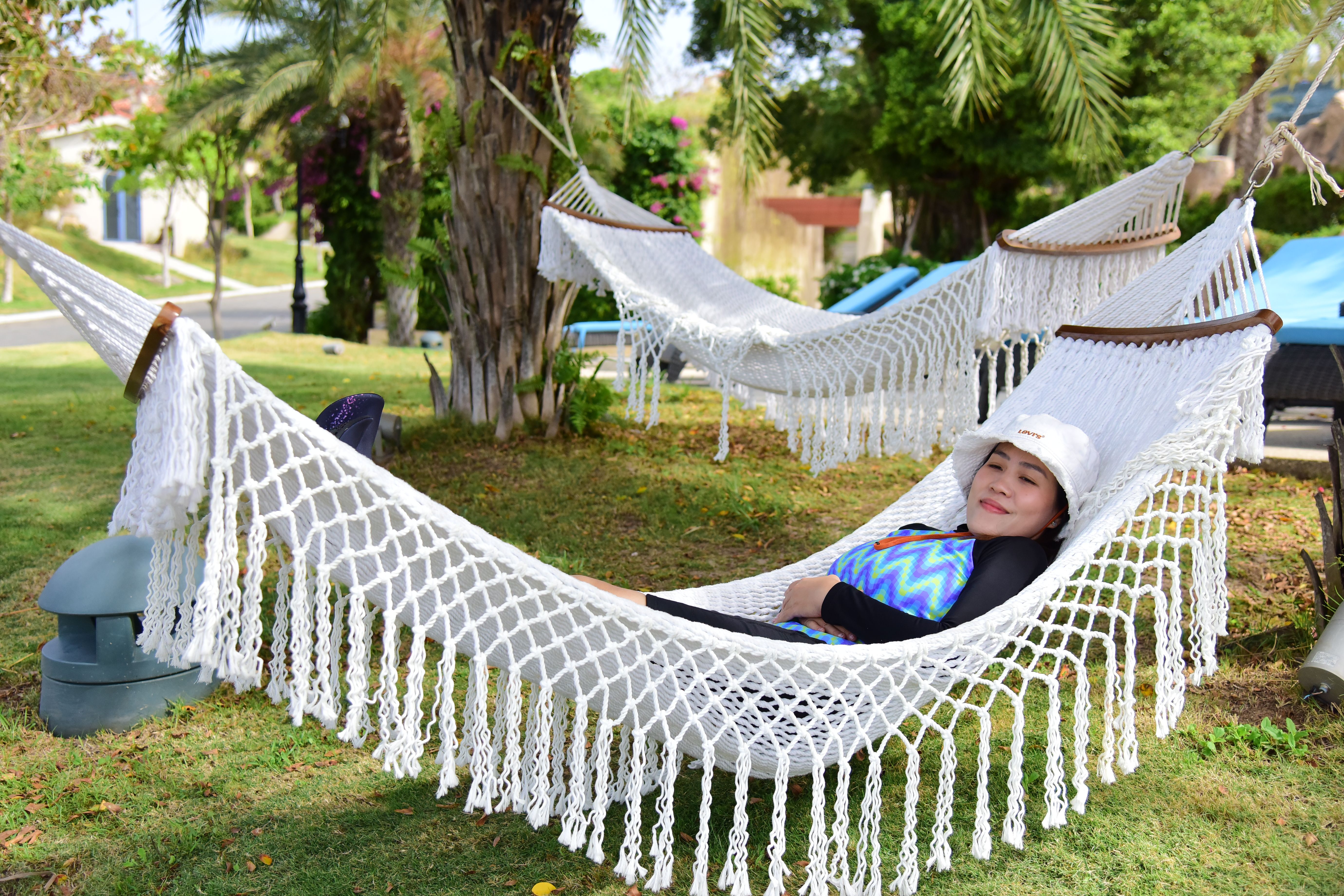 A woman enjoys a peaceful afternoon on a hammock in a sunny park with palm trees.