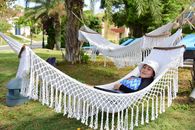 A woman enjoys a peaceful afternoon on a hammock in a sunny park with palm trees.