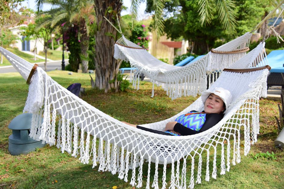 A woman enjoys a peaceful afternoon on a hammock in a sunny park with palm trees.