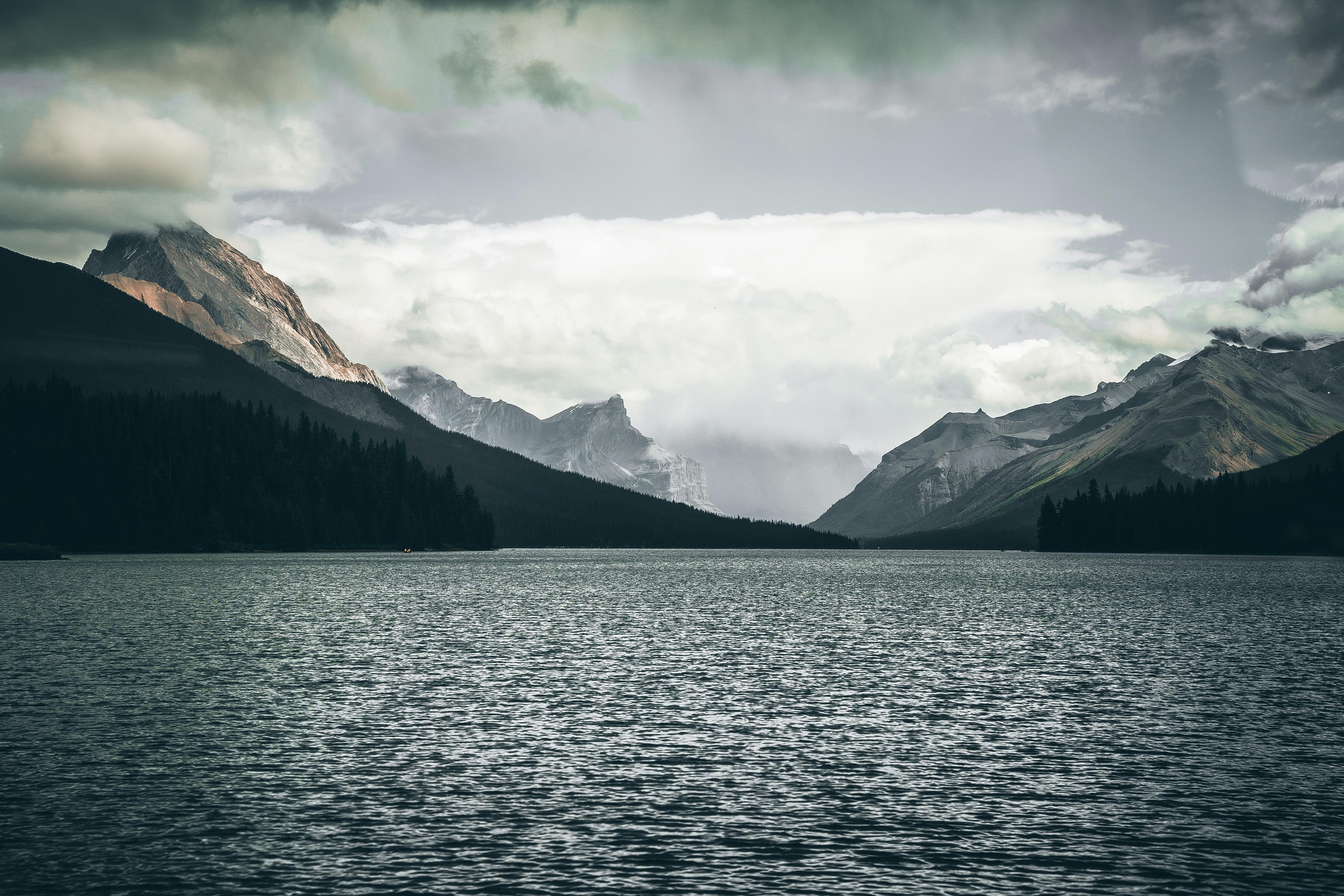 Gratis Danau alpine yang tenang dikelilingi oleh pegunungan menjulang tinggi di bawah langit berawan. Foto Stok