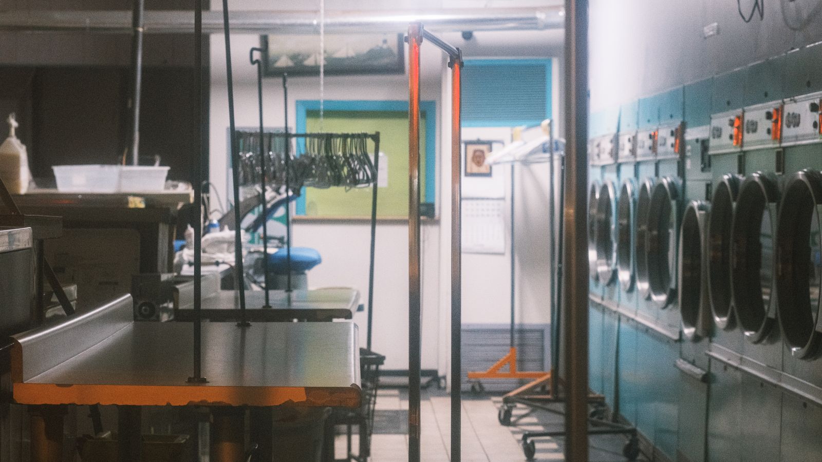Commercial laundry room: blue machines, folding tables, hanging racks