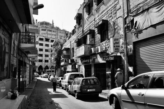 Monochrome image of a busy urban street with pedestrians and parked cars.