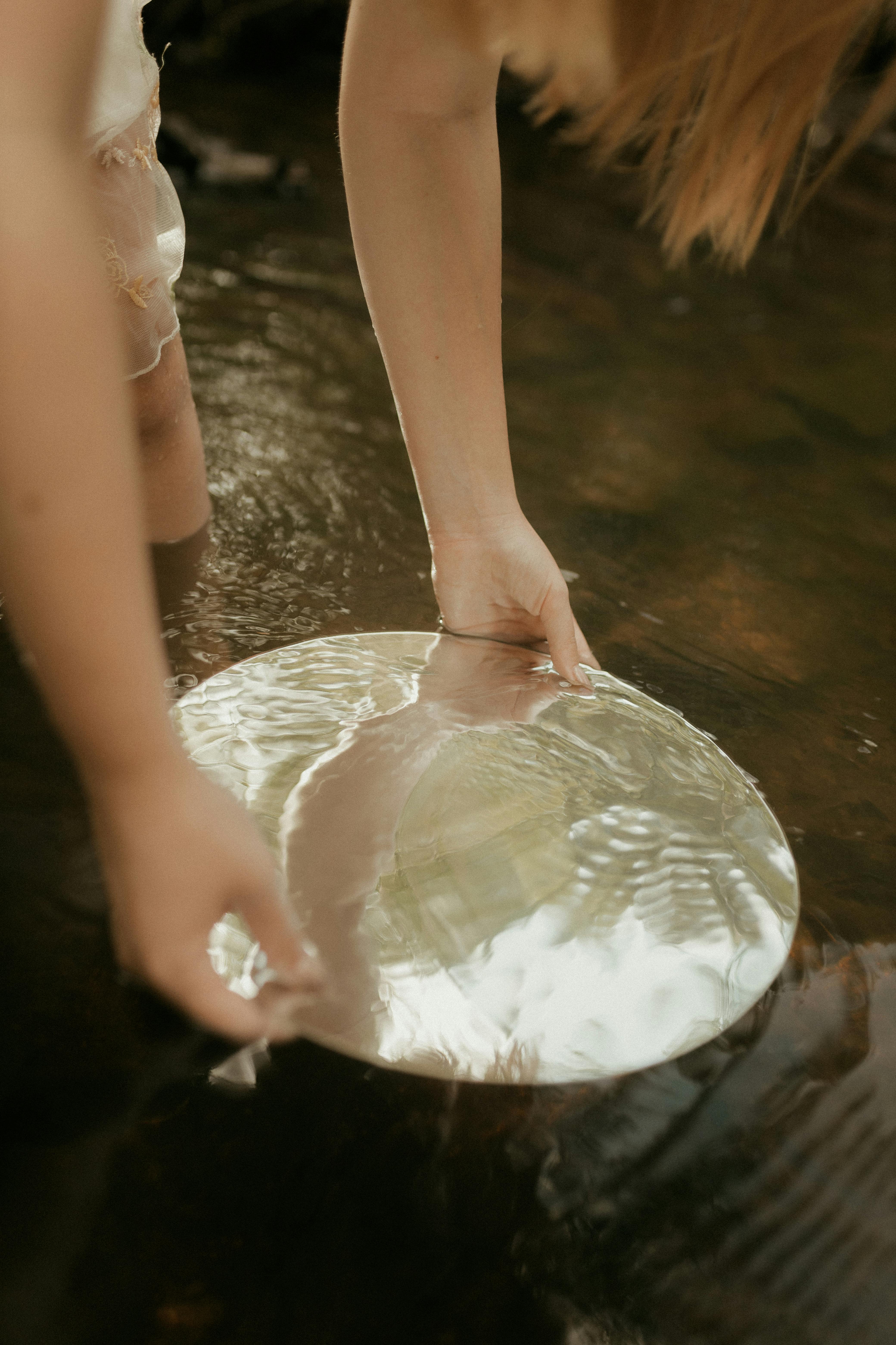 A person holding a reflective disc in a calm stream, creating a serene and artistic scene.