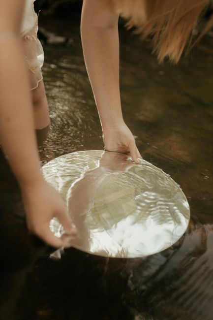A person holding a reflective disc in a calm stream, creating a serene and artistic scene.