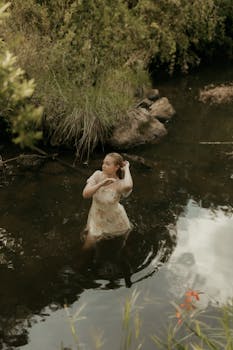 Graceful woman wades in a serene river surrounded by lush greenery. Summer day, nature's beauty.