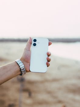 A hand holding a white smartphone at the beach in Rabat during daytime, showcasing modern technology.