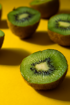 Close-up of fresh kiwi slices on a bright yellow background, emphasizing texture and color contrast.