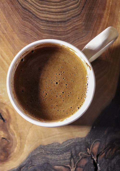 Free A close-up of a steaming cup of black coffee on a rustic wooden table, evoking a cozy atmosphere. Stock Photo