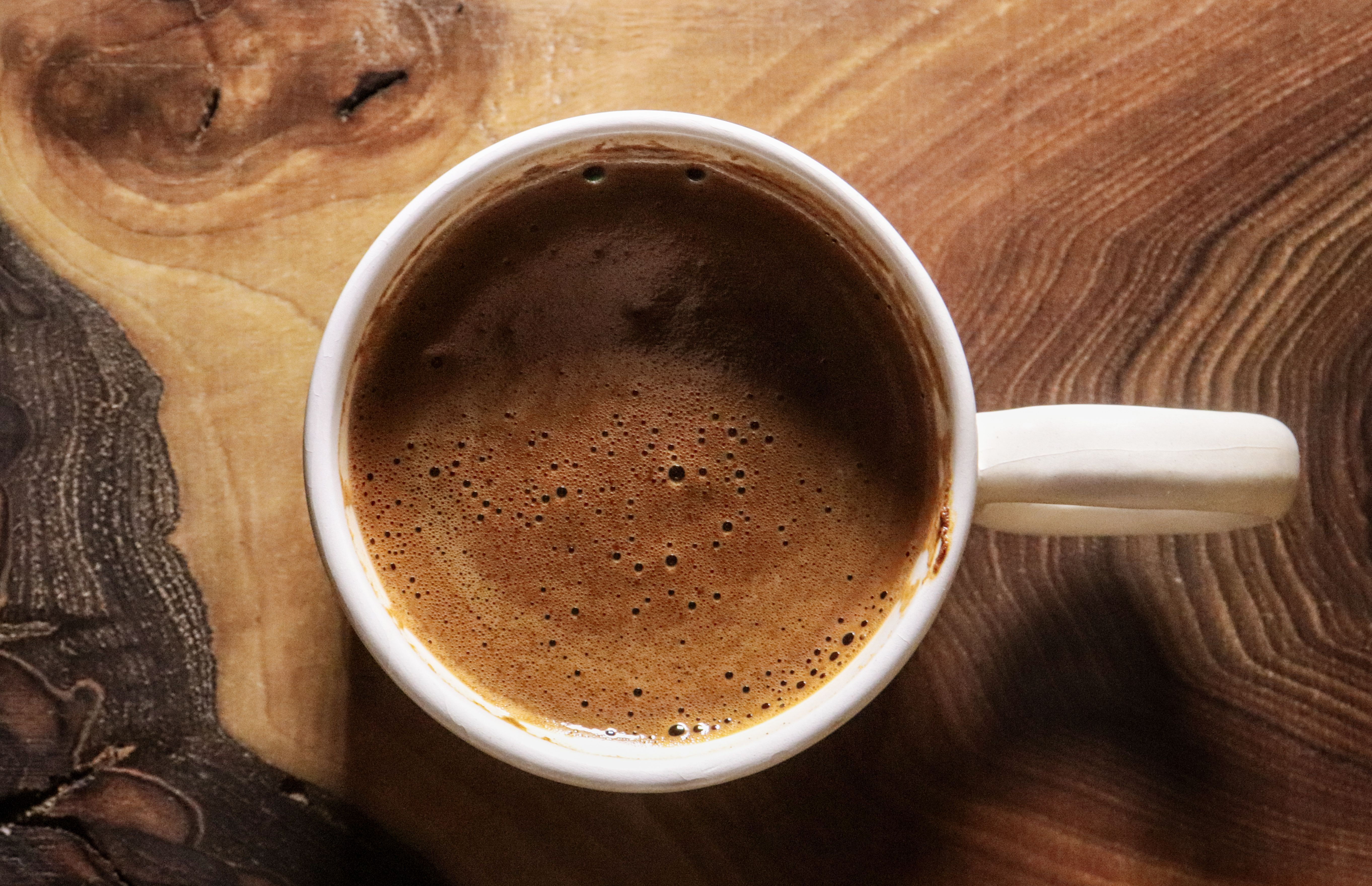 Top view of a freshly brewed coffee in a white mug on a wooden table surface.