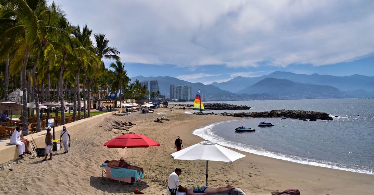 A serene beach view in Puerto Vallarta with palm trees, umbrellas, and a sailboat.