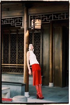 Model posing in red and white attire against a backdrop of traditional architecture.