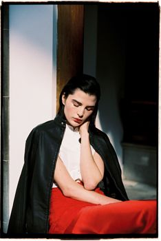 A thoughtful woman in chic attire sitting indoors, captured in a vintage style.