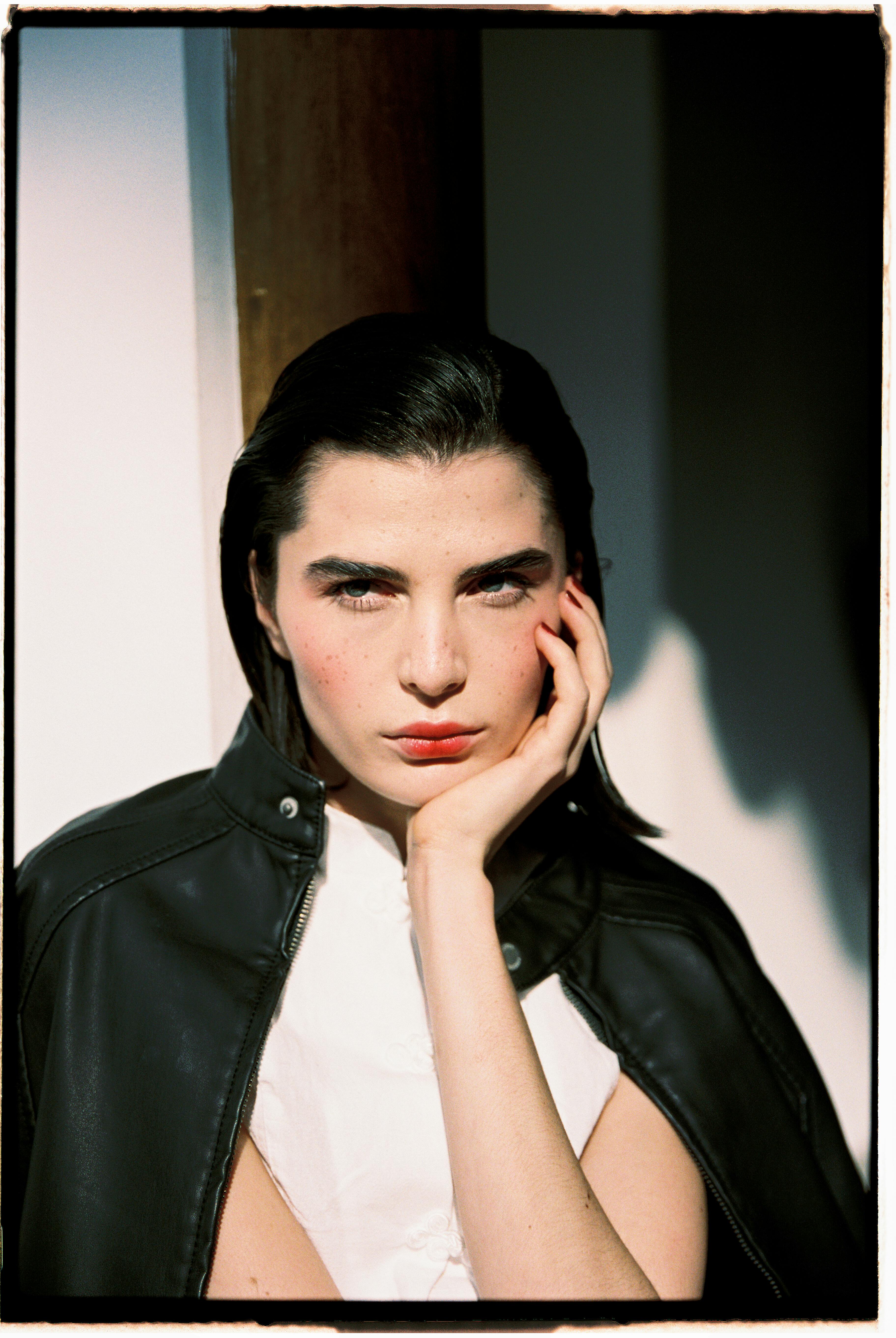 Portrait of a woman in natural light wearing a leather jacket, showcasing bold makeup.