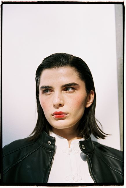 Confident woman in a black leather jacket against a bright background.