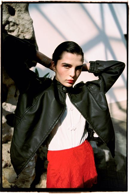 Stylish woman in a leather jacket and red skirt posing outdoors.