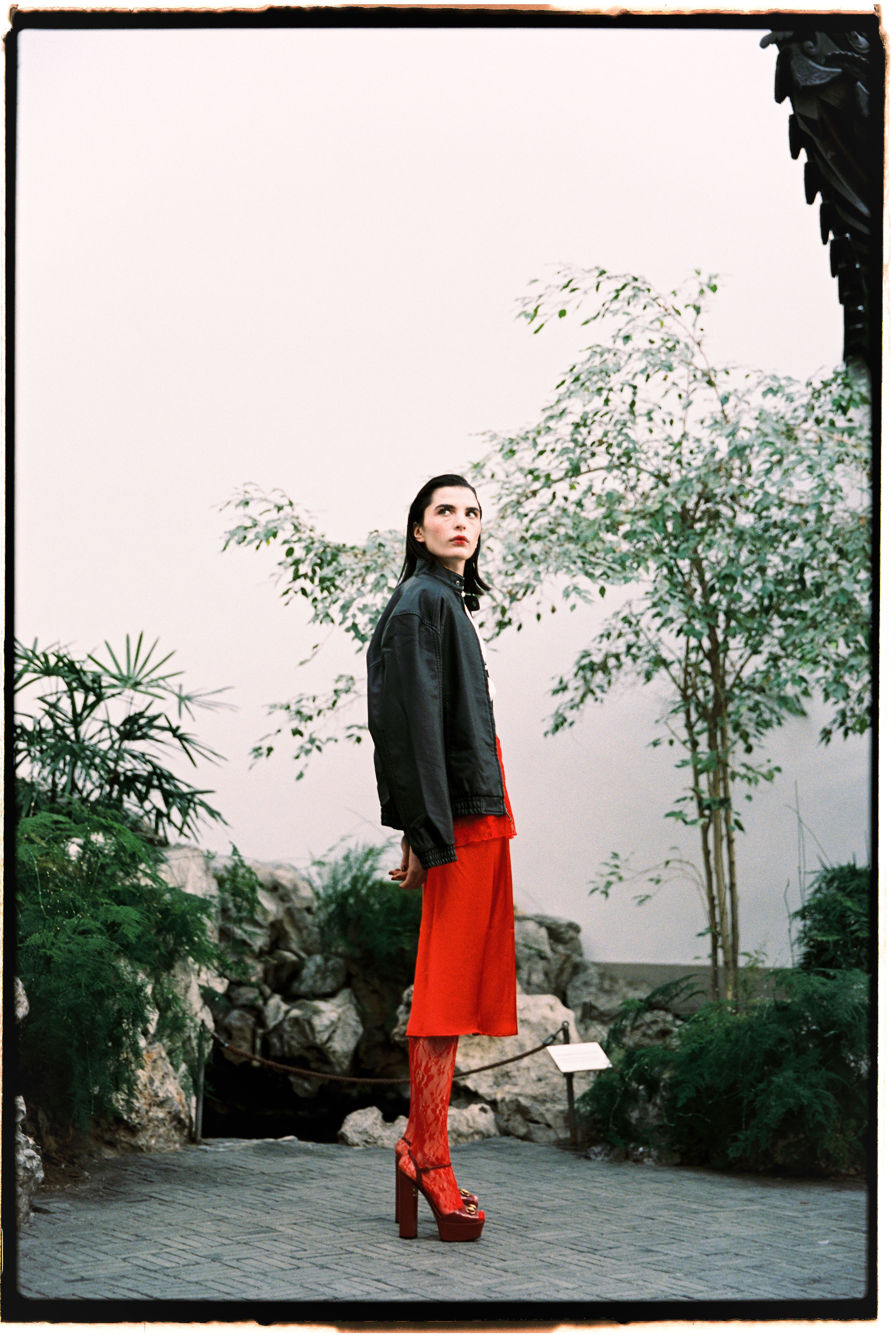 Fashionable woman in red outfit posing indoors with lush greenery.