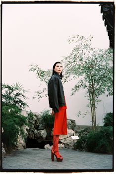 Fashionable woman in red outfit posing indoors with lush greenery.