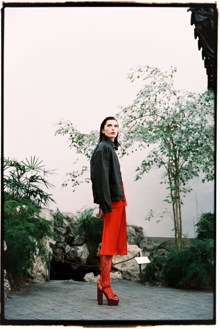 Fashionable woman in red outfit posing indoors with lush greenery.