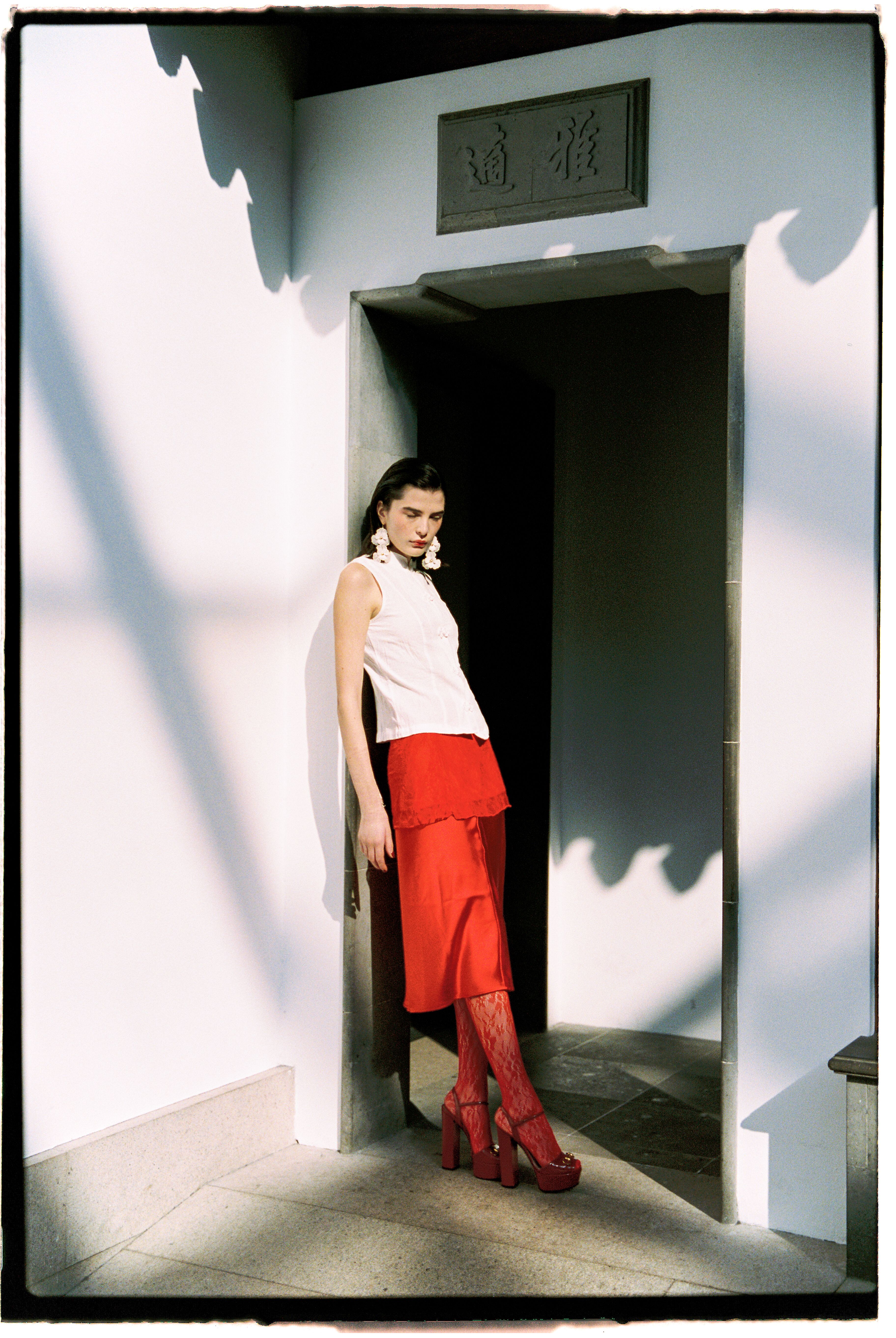 Fashion model in red and white attire posed in a minimalist modern architectural doorway.