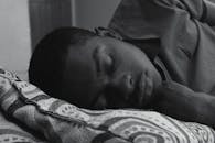 一张黑白照片中，一个男人正安静地睡在卧室的图案枕头上