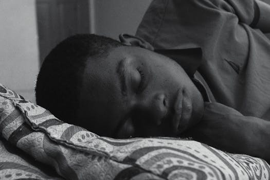 一张黑白照片中，一个男人正安静地睡在卧室的图案枕头上