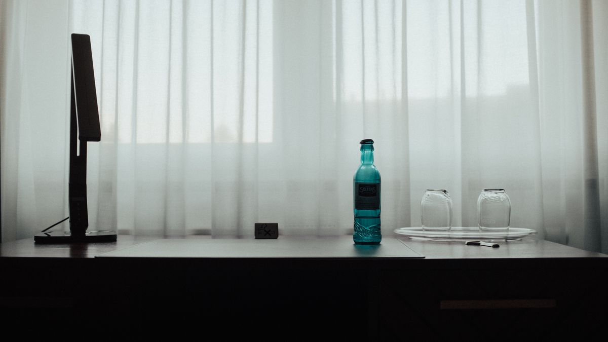 Simple desk with a blue bottle and empty glasses beside a soft lit window.