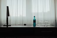 Simple desk with a blue bottle and empty glasses beside a soft lit window.