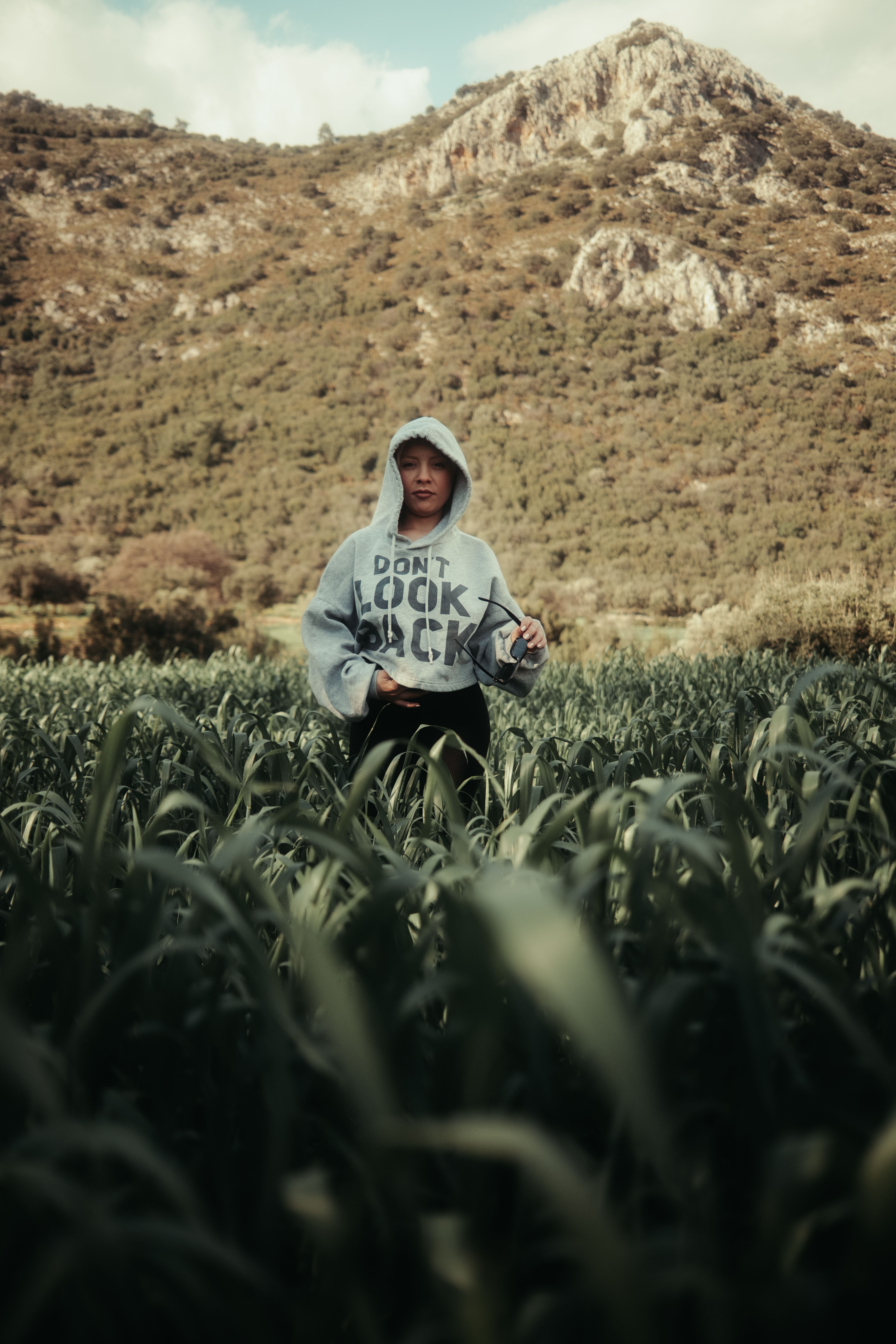 Person in Hoodie Standing in Lush Green Field · Free Stock Photo
